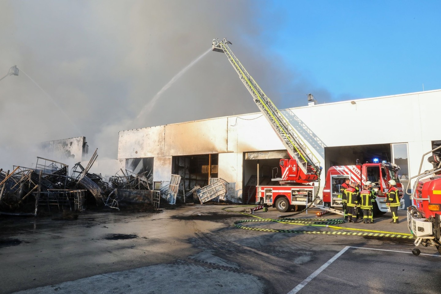 Einsatzkräfte der Feuerwehr stehen während eines Großbrandes auf dem Gelände des Reifengroßhändlers und löschen das Feuer.