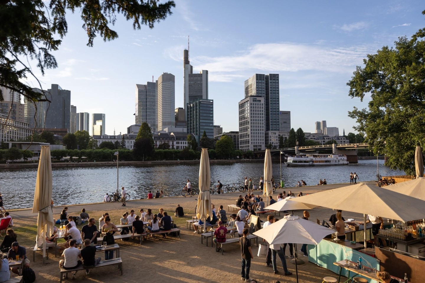 Menschen sitzen in einem Cafe am Mainufer, im Hintergrund die Skyline. In der Gastronomie gibt es unter anderem wegen der Pandemie einen großen Personalmangel.