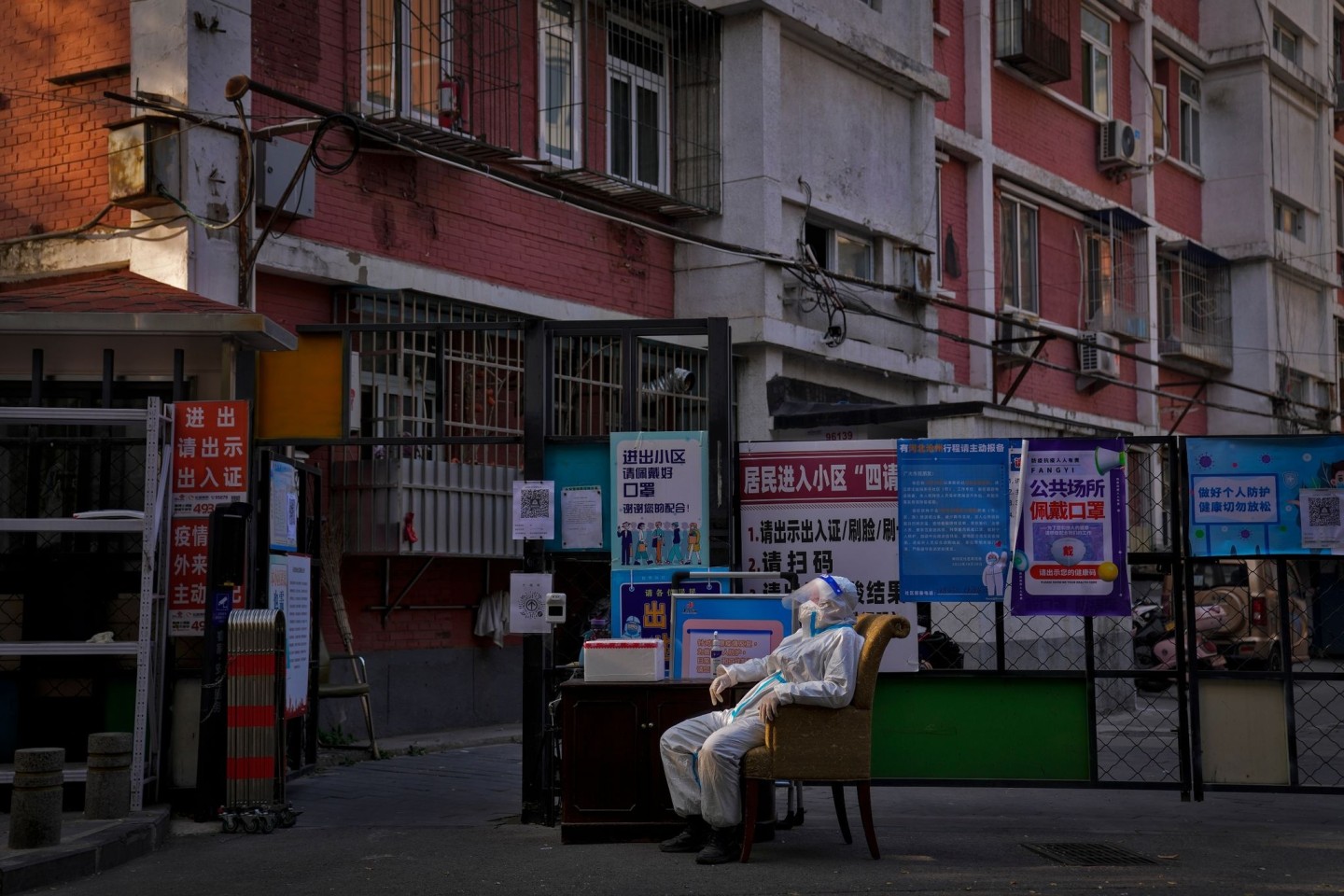 Ein Wachmann im Schutzanzug sitzt an einem Eingangstor zu einem Wohnviertel in Peking.