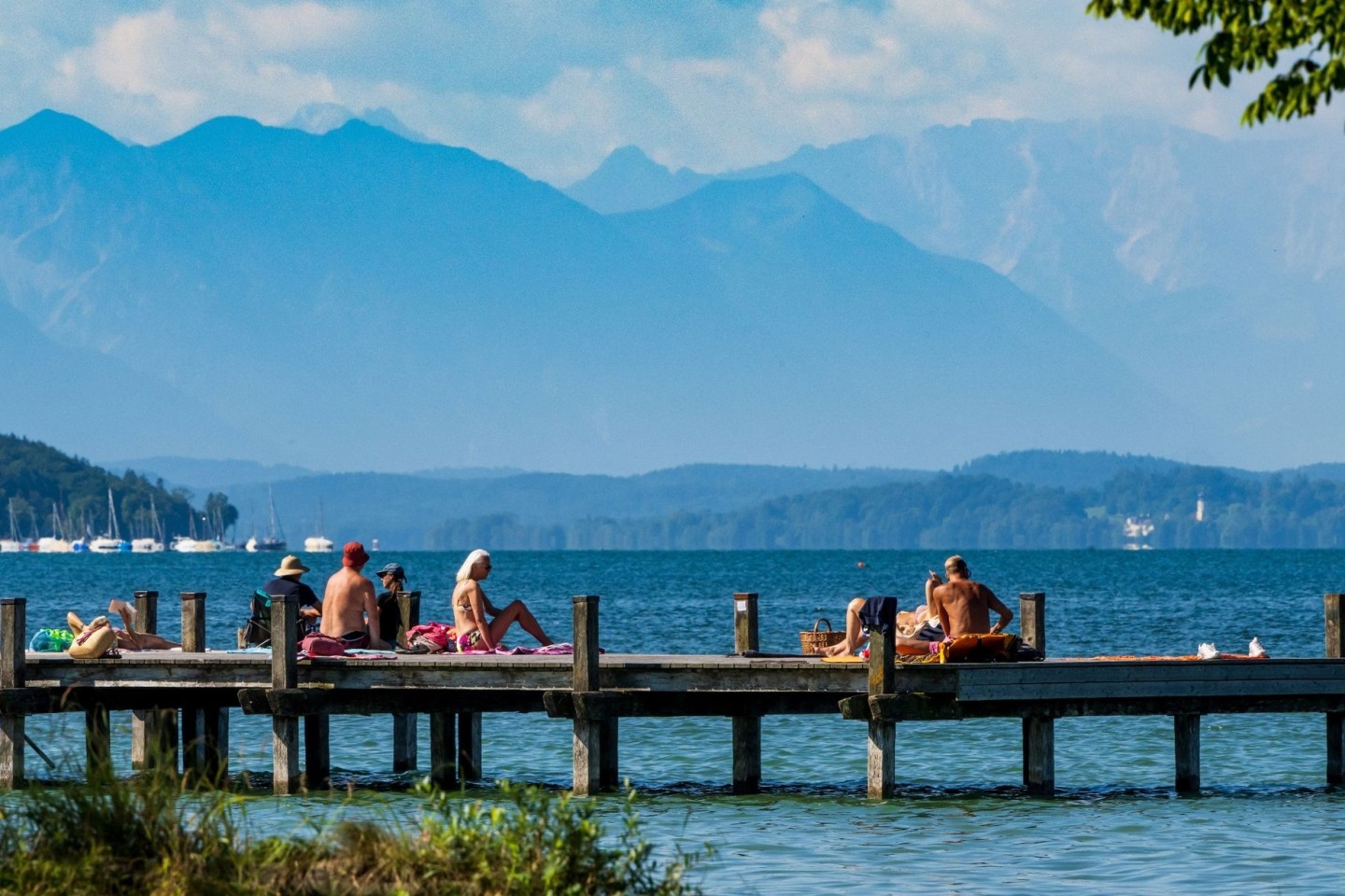 Sonnenhungrige geniessen das warme Wetter auf einem Steg im Starnberger See.