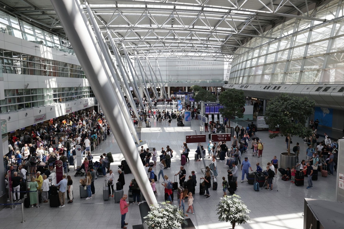 Reisende stehen im Flughafen Düsseldorf in langen Warteschlangen an der Gepäckabgabe.