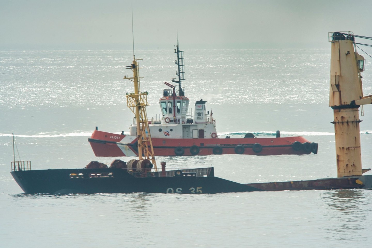 Ein Schlepper liegt hinter dem Frachter, der halb gesunken ist.