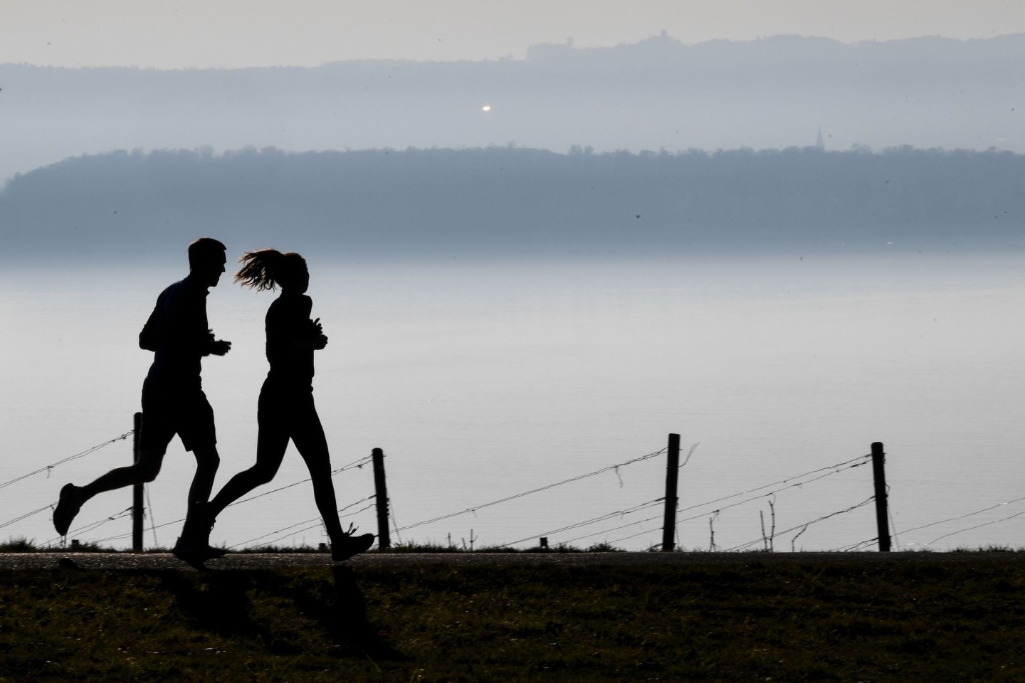 Jogger laufen in Richtung Meersburg, im Dunst dahinter liegt die Stadt Konstanz am Bodensee.