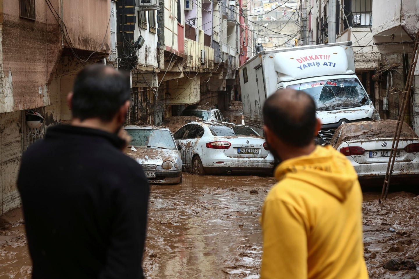 Menschen betrachten Fahrzeuge, die nach heftigen Regenfällen in Sanliurfa im Morast stehen.