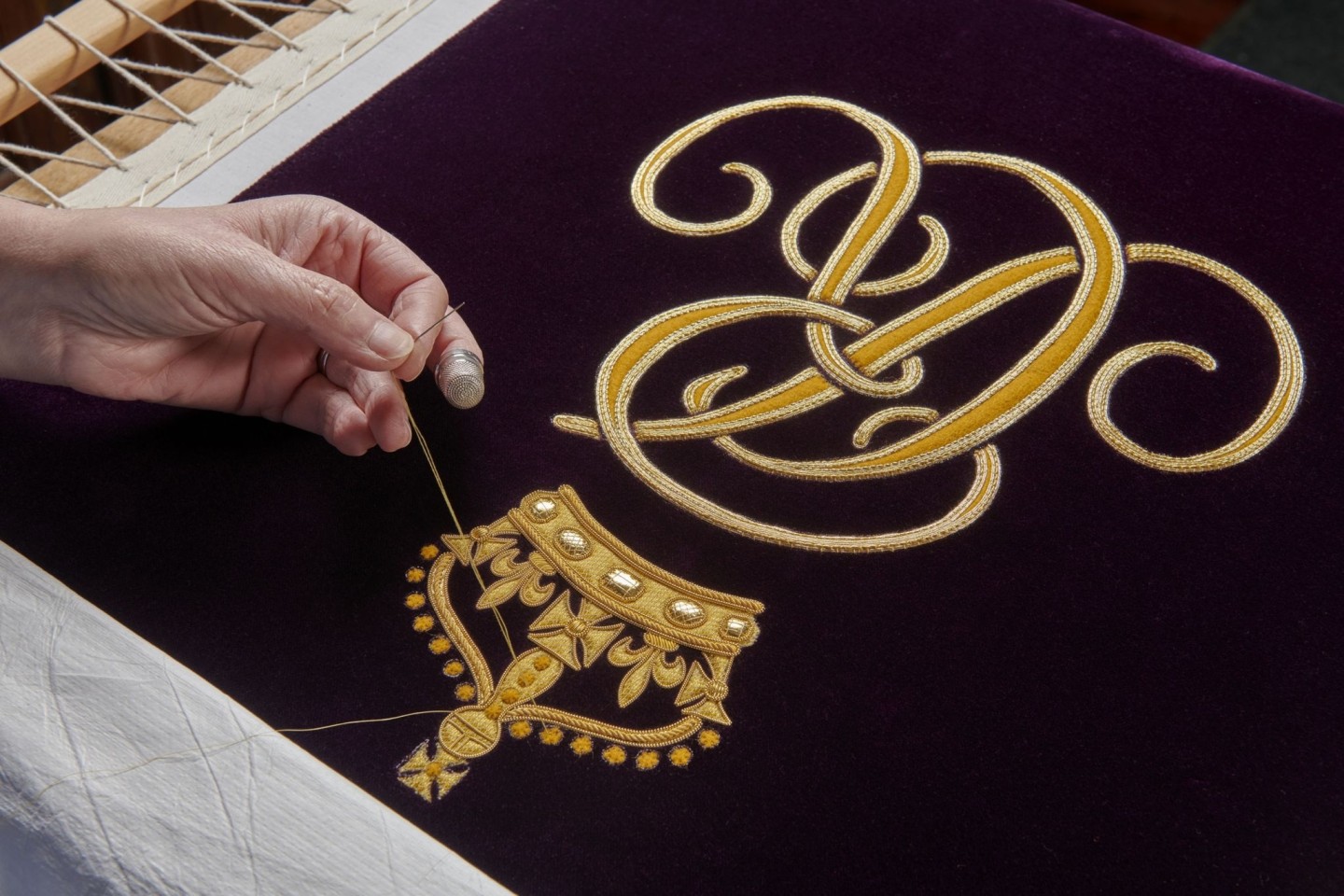 Ein Mitglied der Royal School of Needlework stickt den Schriftzug von Queen Camilla von Hand auf deren Robe.