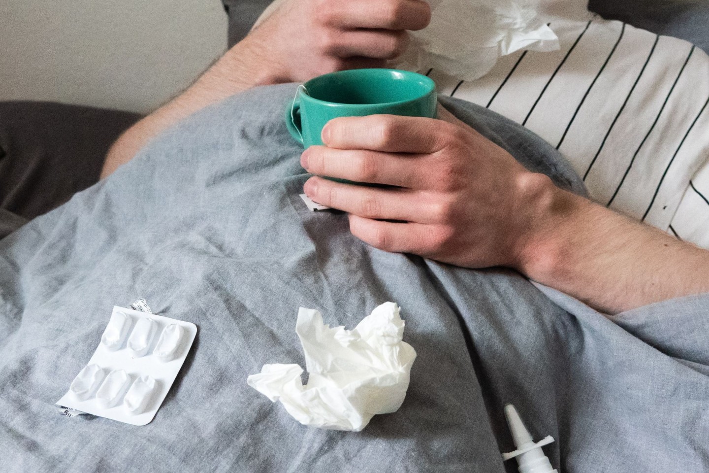 Bettruhe mit Taschentüchern, Teetasse, Nasenspray und Tabletten.