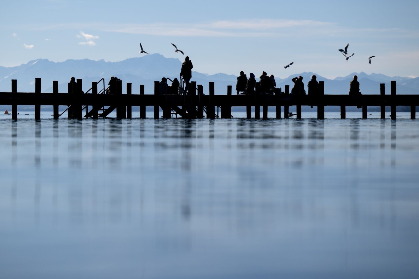 Menschen genießen das schöne Wetter auf einem Steg am Starnberger See.