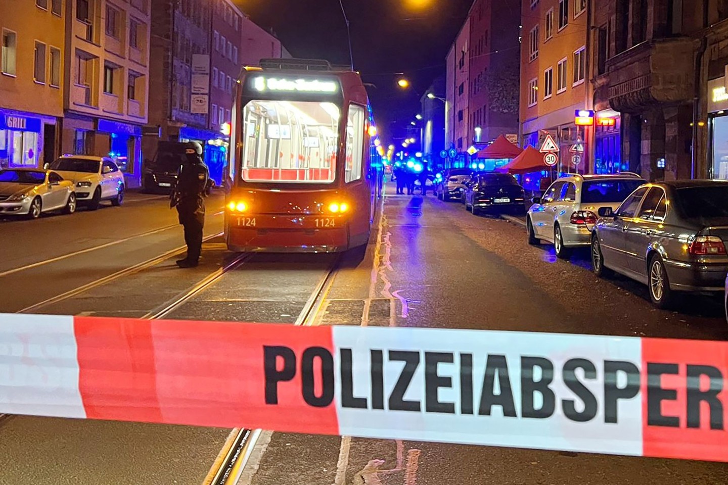 Ein Polizist steht mit einer Maschinenpistole hinter einer Polizeiabsperrung.