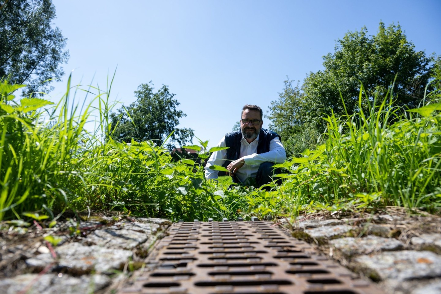 Jochen Meissner, Leiter der Abteilung Stadtentwässerung und Wasserbau der Stadt Neu-Ulm, hinter der Regenrinne einer Straße.