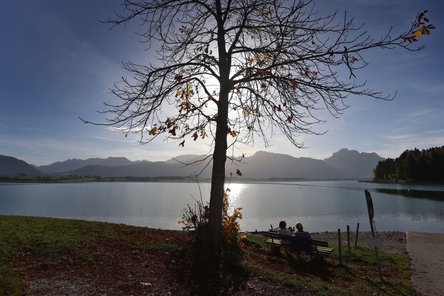 Ausflügler genießen den Sonnenschein am Ufer des am Alpenrand gelegenen Forggensees.