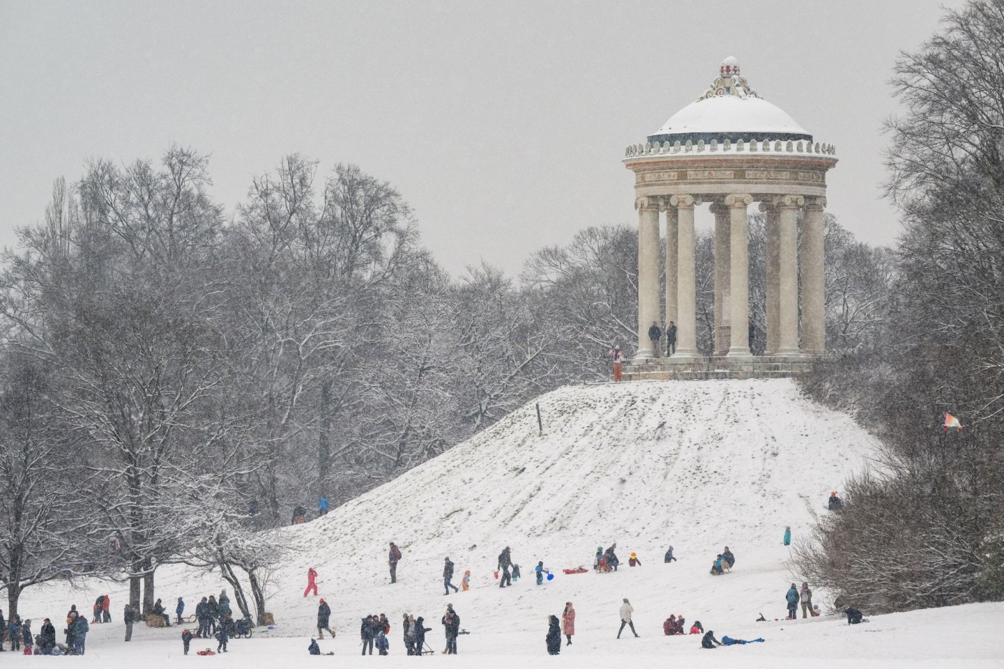 Kinder und Erwachsene rodeln am Hügel des Monopteros im Englischen Garten in München.