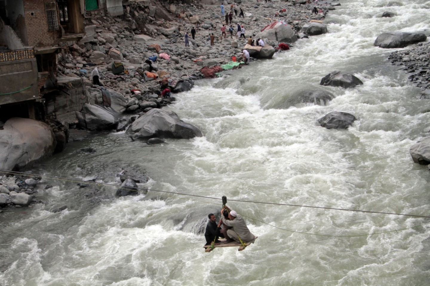 Menschen überqueren einen Fluss im pakistanischen Bahrain mithilfe einer Seilbahn. Verheerende Überschwemmungen haben in dem Land schon mehr als 1160 Menschen das Leben gekostet.